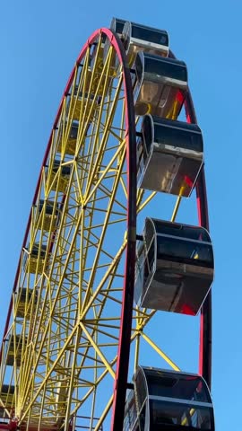 Imposing Ferris wheel with a vibrant yellow and red structure, featuring fully enclosed passenger cabins set against a bright clear blue sky.