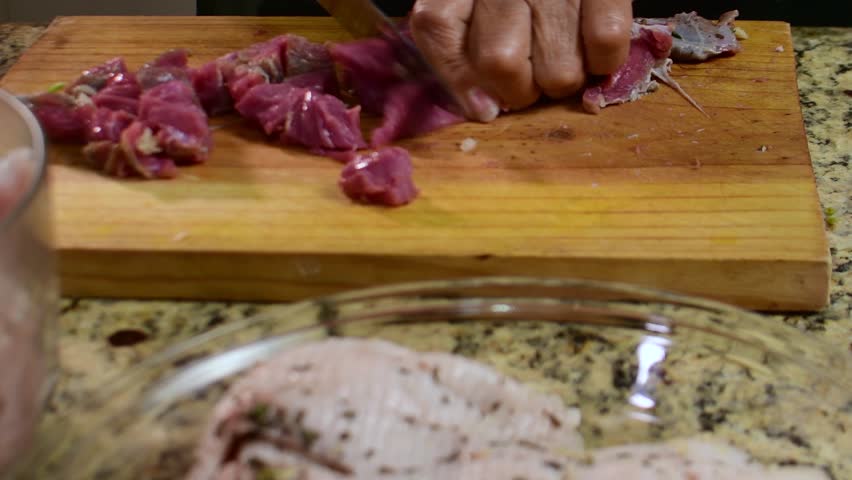 Close-up of hands cutting raw meat into small pieces on a cutting board, home kitchen preparation, traditional cooking, fresh ingredients, artisanal process.