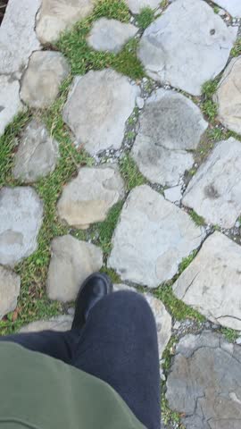 Close up view of a womans foot stepping on an uneven stone path. The scene shows careful walking on rocky ground, balance during movement, textured pavement, and forward motion along an outdoor route.