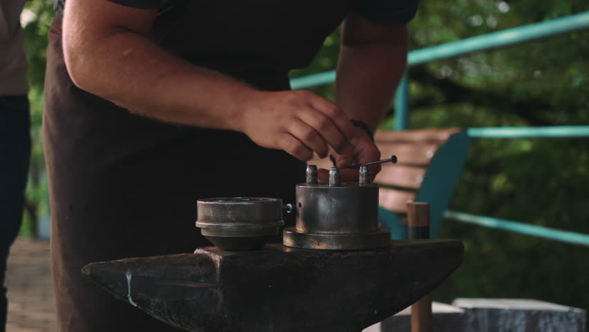 Caucasian Blacksmith Hands Arranging Metal Molds On Anvil Outdoor Studio, Careful Assembly With Hammer