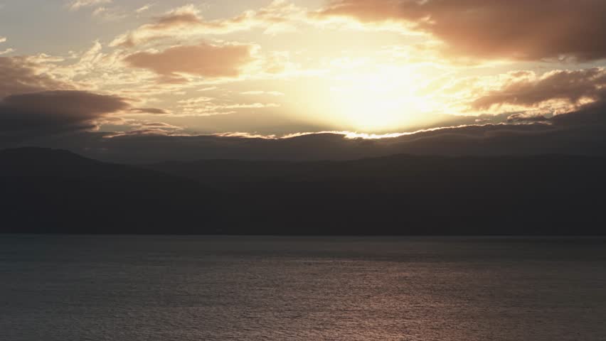 Cinematic view of golden sun rays piercing through heavy storm clouds over the Dead Sea and Jordan mountains during a gloomy winter sunset.