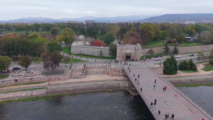 Helix drone movement over Niš reveals the fortress walls and main bridge spanning the river, showcasing the historic architecture and flowing urban landscape.