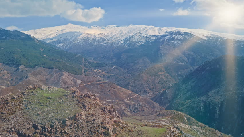 Majestic Sierra Nevada mountain range in southern Spain with bright sunlight over green valleys and snow capped peaks breathtaking natural scenery peaceful wilderness under blue sky aerial view travel