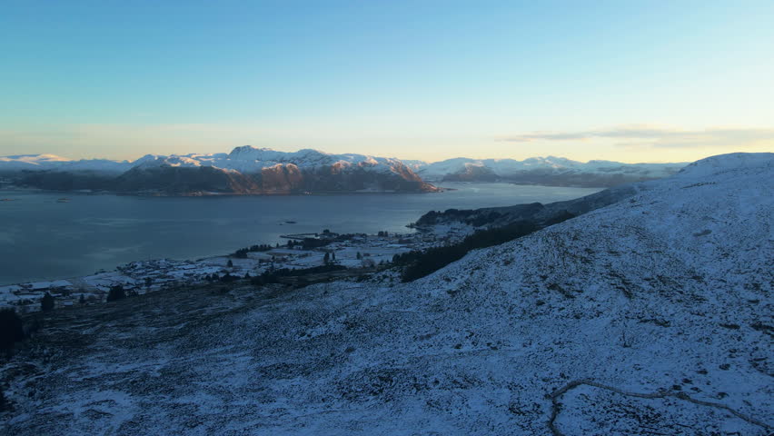 Scenic drone shot over a small town in Norway with a beautiful sunrise shining on the mountains in the far on a cold winter day in Norway