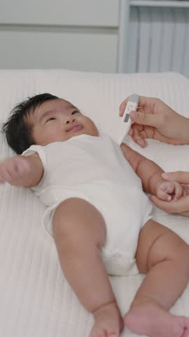 Closeup newborn baby boy lying on white blanket while thermometer placed under armpit, health checkup process in cozy clinic, legs and hands moving slightly during temperature measurement