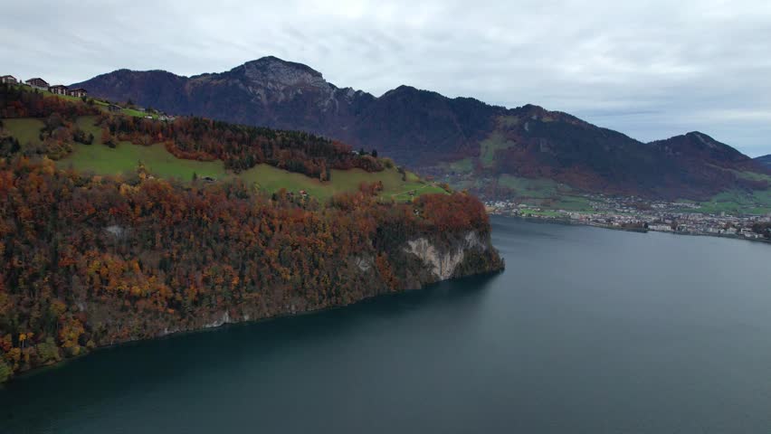 Panoramic aerial video capturing the majestic Swiss Alps mountain range and the calm waters of Lake Lucerne on a cloudy autumn day.