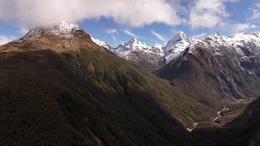 Aerial drone view of majestic snow-capped mountain peaks on the way to Milford Sound. The dramatic landscape features a lush valley below. Ideal for adventure and nature concepts, New Zealand