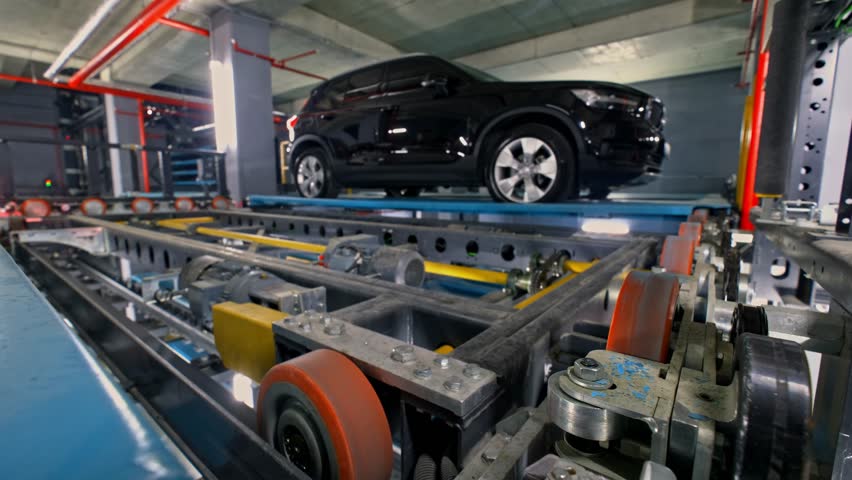 A robotic parking platform transporting a vehicle inside an automated smart parking system, featuring metal rails, mechanical structures, and high-tech movement in a multi-level facility.