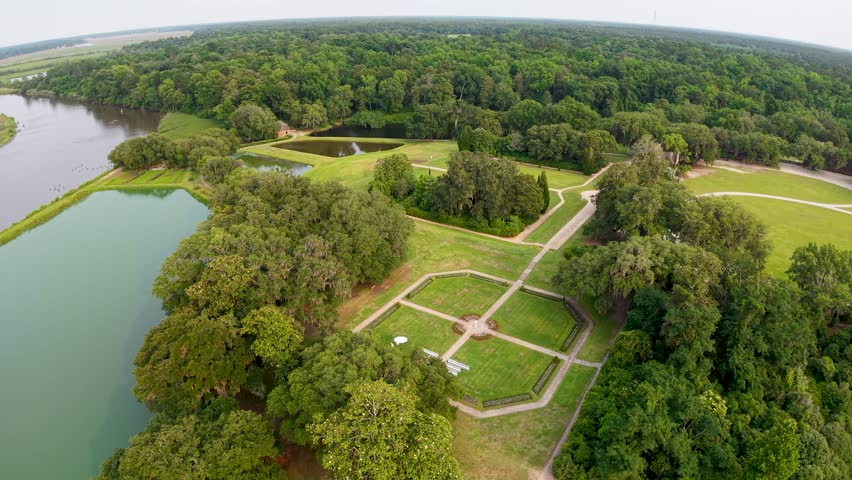 Aerial drone footage glides over formal geometric gardens and reflecting pools at Middleton Place Plantation in Charleston South Carolina showing intersecting paths green lawns and surrounding trees.