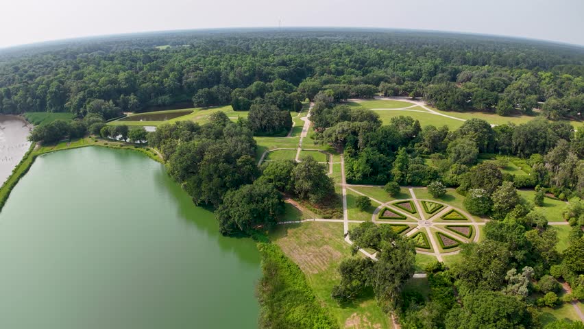 Drone footage captures a tranquil green pond with a formal cross-shaped walkway at Middleton Place Plantation near Charleston, SC, surrounded by lush trees and manicured lawns.
