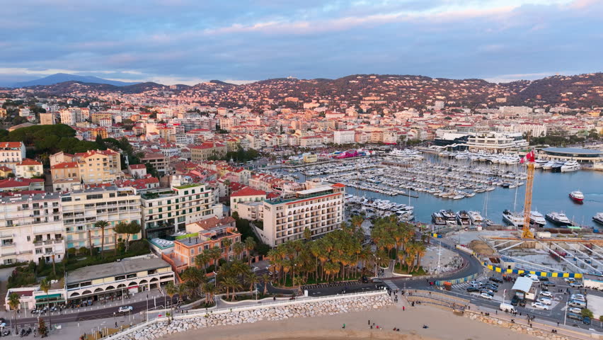 Aerial Footage Showcases Vibrant Waterfront Illumination Against City And Mountain Skyline Backdrop. Cannes. France