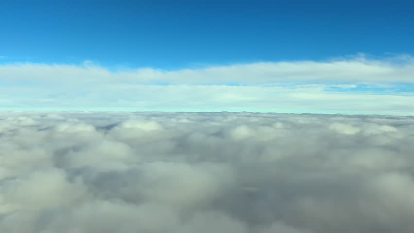 Cockpit view while descending through an endless layer of stratus clouds under a blue sky.