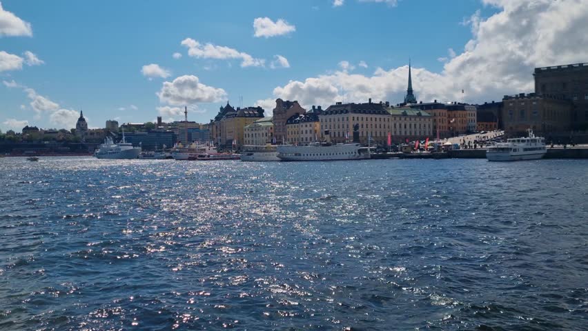 View across Stockholms ström toward historic waterfront houses in central Stockholm, Sweden, with boats on the water and a bright, sunny sky highlighting the classic cityscape