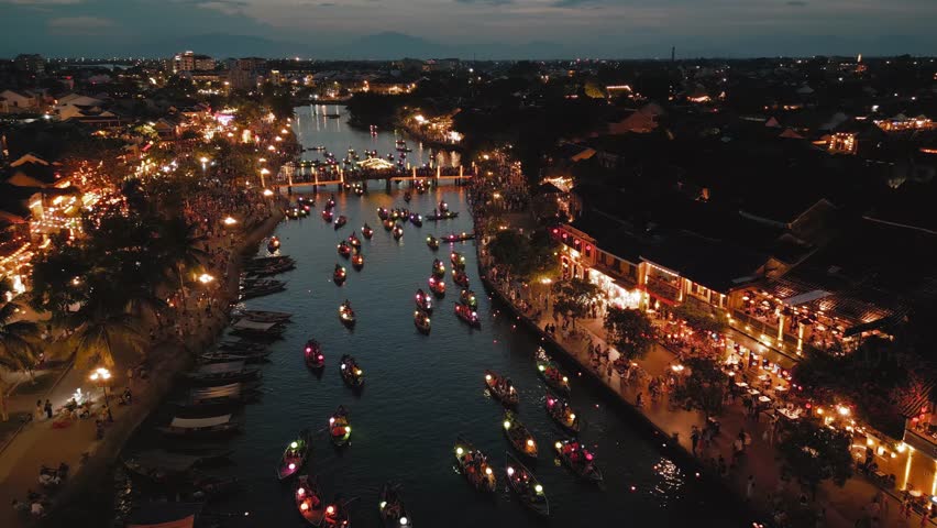 Drone flyover of Hoi An s lantern boat festival at night with crowds and glowing lights. Perfect for showcasing cultural vibrance, tourism, and traditional Vietnam in stock video. 