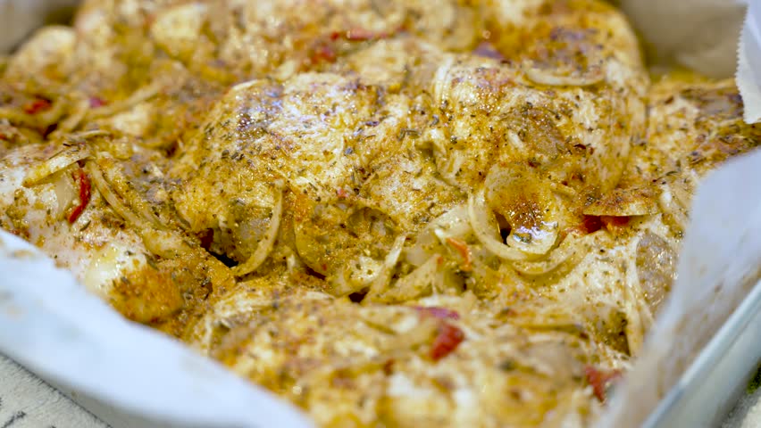 Close-up of seasoned raw chicken pieces with onions ready for baking in a pan.