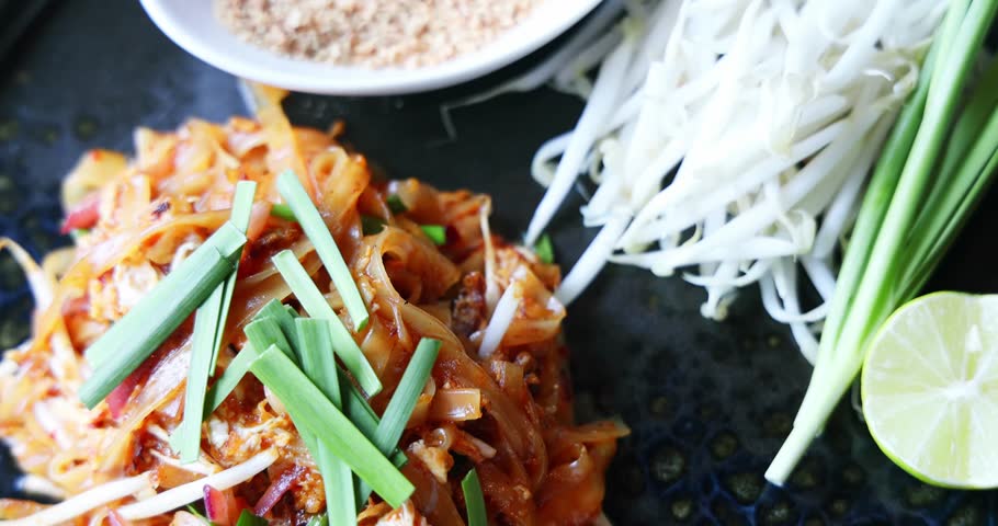 Pad Thai noodles served with fresh garnishes in close-up. Slow motion. Authentic Thai cuisine concept. Appetizing, savory, traditional. High-speed video.