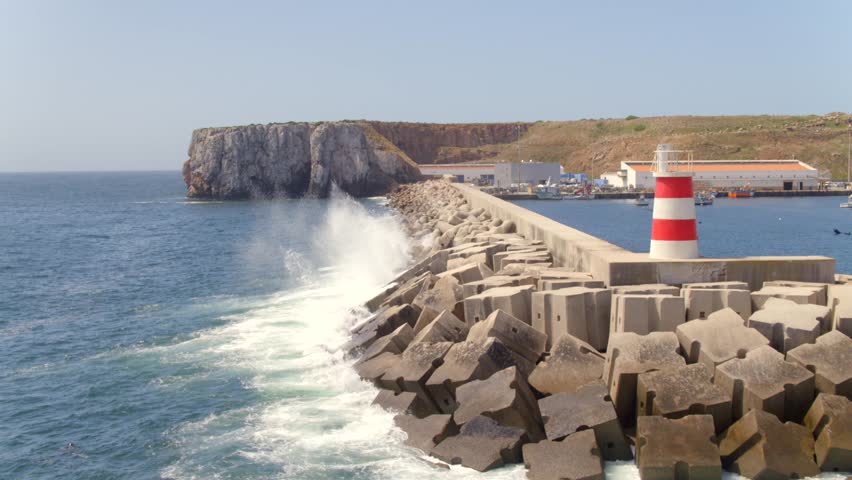 Sagres port breakwater with lighthouse and waves, Algarve, Portugal