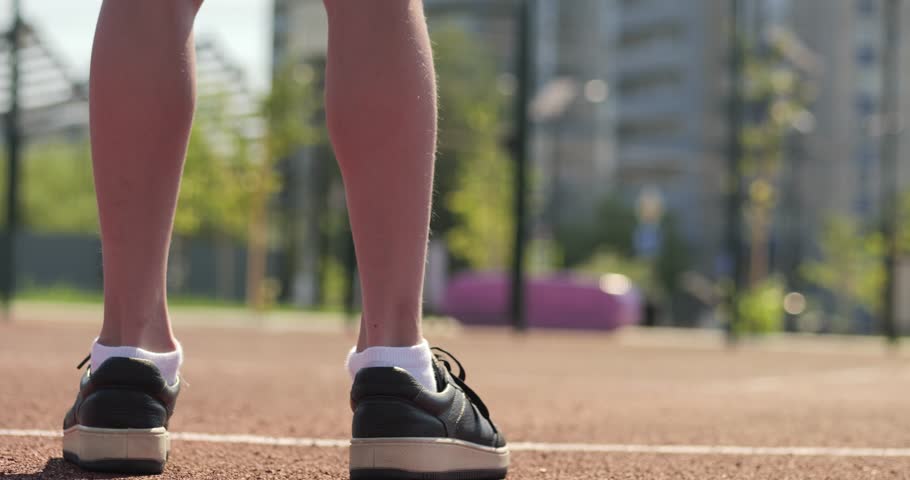 Close up of child legs on outdoor court in sunny day. Basketball moment shows focus and readiness before play. Minimal basketball scene highlights kids sport lifestyle. Child boy basketball player.