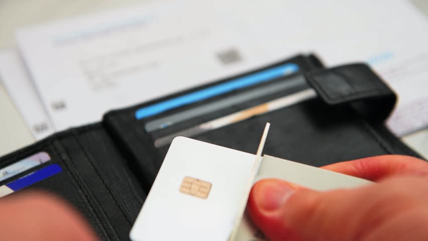 A close up of a person cutting up a bank credit card with an open purse and credit card bills in the background.