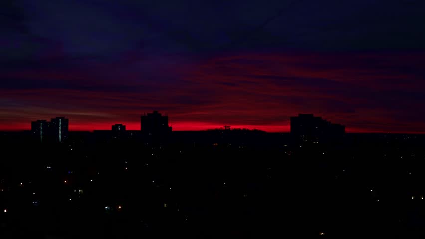 A Vibrant Cityscape Timelapse Transitions From A Deep Red Dawn To A Bright Purple-hued Morning Sky Over A Silhouetted Urban Horizon