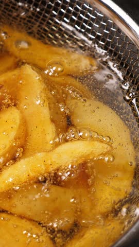 Cooking potatoes wedges in deep fryer. Closeup. Vertical footage