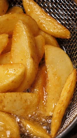 Cooking potatoes wedges in deep fryer. Closeup. Vertical footage