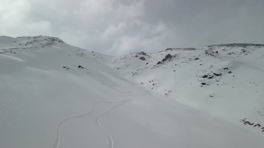 Aerial perspective of winding ski trails cutting through untouched snow in Gulmarg, Kashmir. The vast, unspoiled mountain terrain highlights the thrill and beauty of off-piste skiing