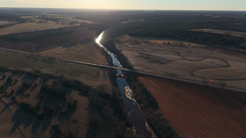 Aerial view of a winding river reflecting the winter sunset as it flows through red dirt farmland in rural Oklahoma.