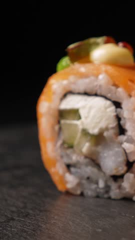 Sushi rolls on black platter over dark background, closeup. Japanese cuisine. Vertical footage