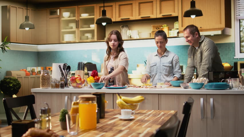 Tween daughter taking a family photo of her and parents during cooking time, smiling for a picture while they prepare homemade pizza in the kitchen. Fun weekend activity together. Camera A.