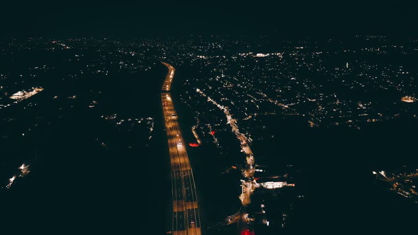 Aerial night view of a city highway with moving traffic and glowing street lights. Urban landscape captured by drone, showing transportation, infrastructure, and city life after dark.