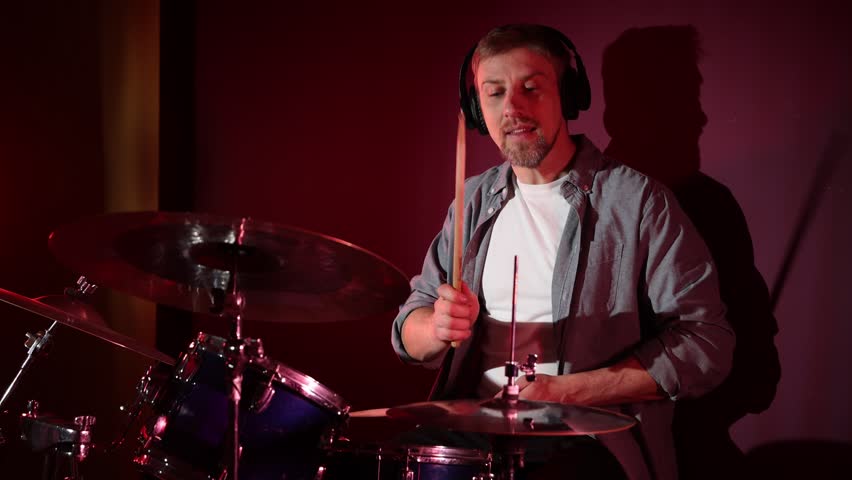 Man in headphones playing drums with drumsticks in studio