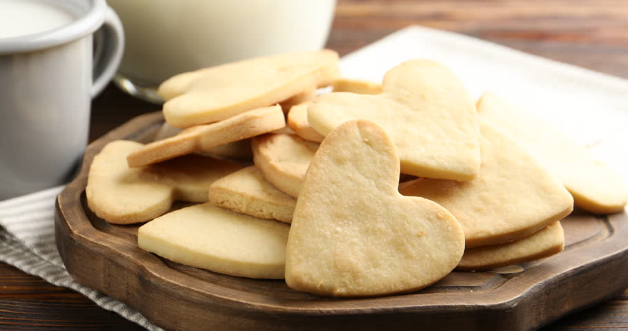 Woman taking tasty heart shaped butter cookie from board at wooden table, closeup