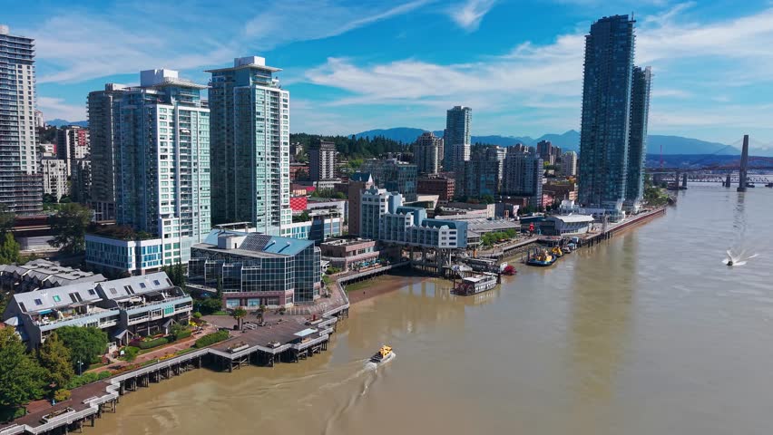 Drone footage of boats traveling along the Fraser River past the modern skyline of New Westminster, British Columbia, with high-rise buildings, and the Pattullo Bridge in the background