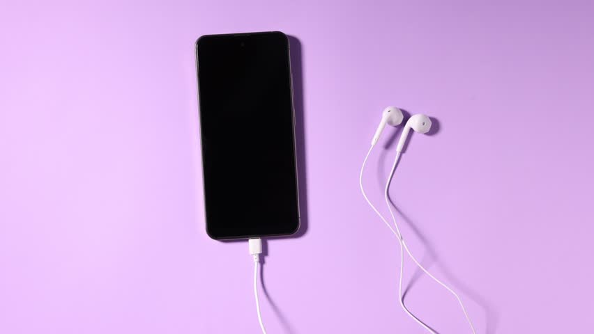 Woman taking smartphone with earphones from lilac background, top view