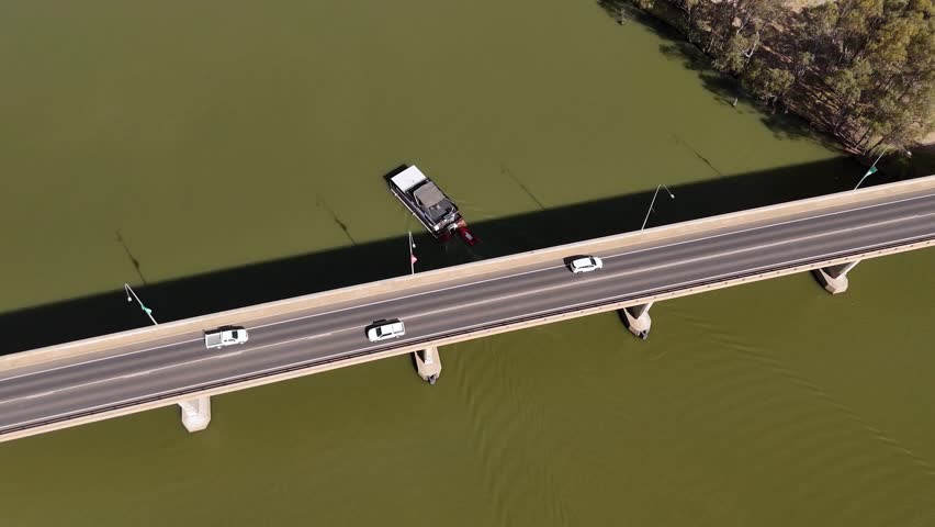 Drone pullback above bridge crossing wide green river with moving traffic in bright daylight, Mildura, Australia