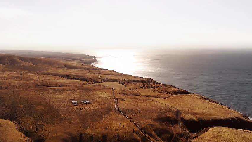 Drone panoramic overview of gentle sloping cliff edge with ocean haze softening distant horizon, Australian establishing landscape