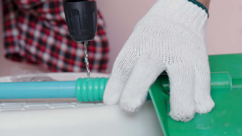 Close-up hand of man to repair the plastic dustpan with using a cordless drill hole a plastic PVC pipe.
