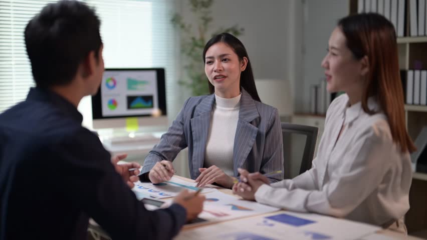 Three people are sitting at a table with papers in front of them. One of the people is a woman