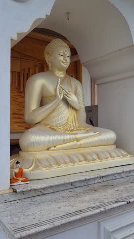 Vertical shot of a Buddha statue at Parewi Duwa Temple in Matara, Sri Lanka, with rain falling, highlighting the serene atmosphere and the temple’s spiritual and tropical setting