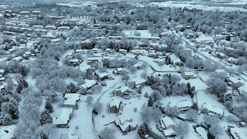 American suburban neighborhood covered in fresh snow, showing quiet residential streets, houses and trees. Calm winter landscape from above. Aerial backwards wide shot.