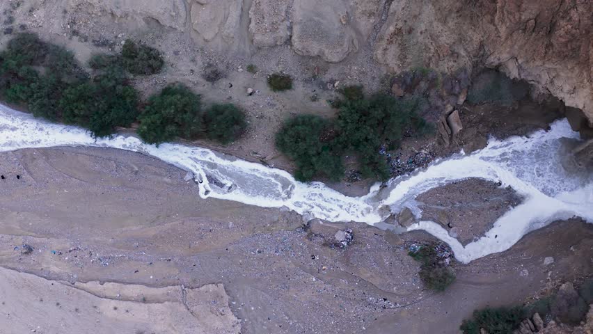 Top down aerial drone view of the Kidron River flowing with muddy flash flood water and cascading over a cliff in the Judean Desert, Israel.