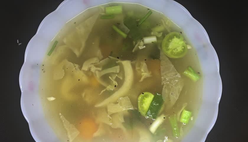 A delicious and visually appealing video featuring a bowl of steaming meatball or vegetable soup. The clear broth is served in a distinctive Imperial Glass bowl with yellow, red, and white floral patterns, making the scene both a foodie's delight and a collector's dream of 1970s Americana.