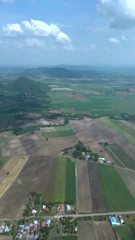 This aerial view captures a serene rural landscape with patchwork farmland, a small village, and a vast expanse of green fields under a blue sky with fluffy white clouds. The scene exudes a sense of peacefulness and natural beauty, inviting the viewer to explore the tranquility of the countryside. Perfect for use in projects related to agriculture, sustainability, travel, and outdoor recreation.