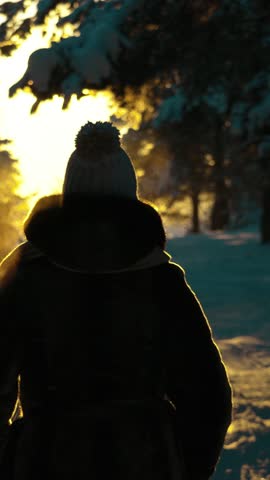 A young girl in warm clothes walks through a winter forest at sunset. Warm steam comes out of the girl