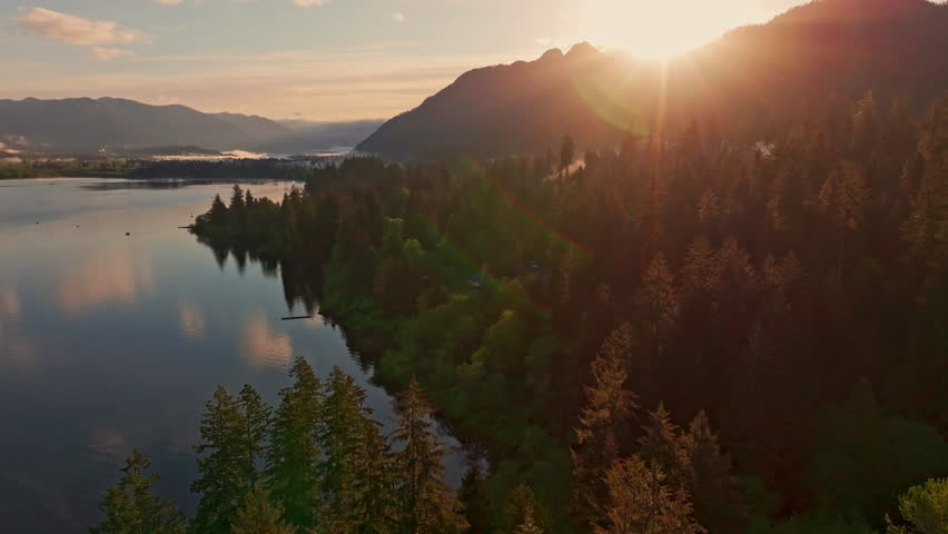 Aerial drone view of Lake Quinault at golden hour, capturing calm water, warm sunrise light, and surrounding rainforest in Olympic National Park. Ideal for nature and landscape footage.