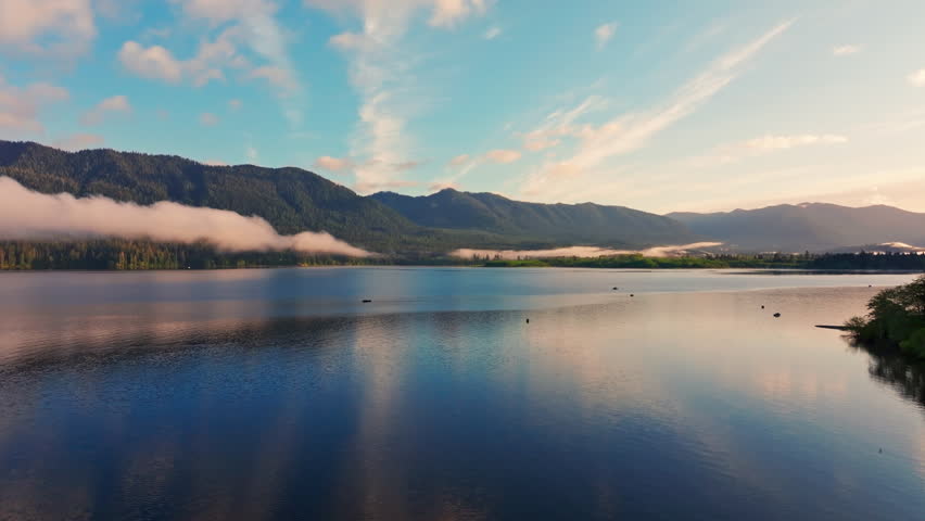 Aerial drone view of Lake Quinault at golden hour, capturing calm water, warm sunrise light, and surrounding rainforest in Olympic National Park. Ideal for nature and landscape footage.