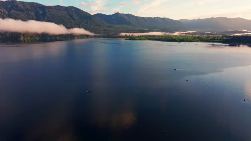Aerial drone view of Lake Quinault at golden hour, capturing calm water, warm sunrise light, and surrounding rainforest in Olympic National Park. Ideal for nature and landscape footage.