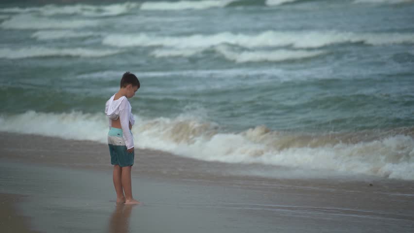 A boy stands on the beach and plays with sea foam