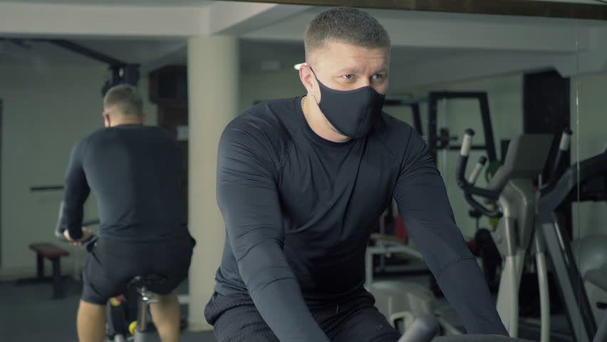 Man exercising on stationary bike wearing a mask in gym setting